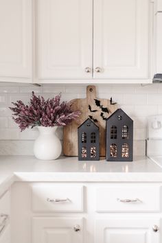 a kitchen counter with two houses on it and a vase full of flowers in the corner