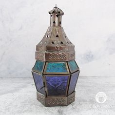 an ornate metal and glass candle holder on a marble counter top with a white wall in the background