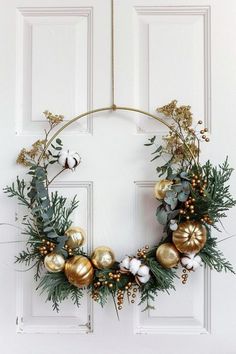 a christmas wreath on the front door with gold ornaments and greenery hanging from it