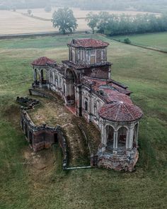 an old abandoned building in the middle of a grassy field with trees and fields behind it