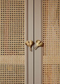 two gold handles on the side of a white cabinet with woven fabric behind it and another door handle that has been made out of brass