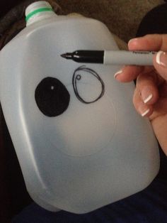 a person holding a pen and writing on a plastic container with a face drawn on it