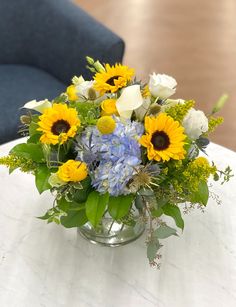 a vase filled with yellow and blue flowers on top of a white table next to a couch