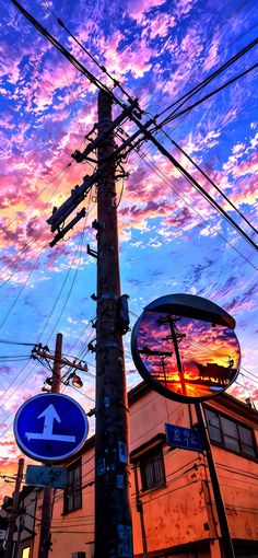 a pole with street signs on it next to a building and telephone wires at sunset