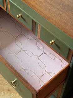 an empty drawer in a green cabinet with wood handles and brass knobs on the drawers