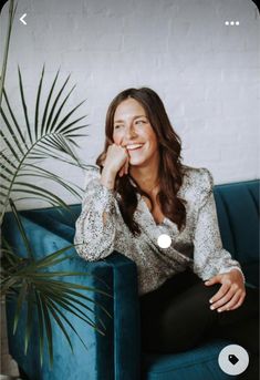 a woman sitting on top of a blue couch next to a potted palm tree