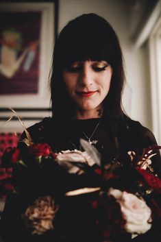 a woman holding a bouquet of flowers in her hands and looking at the camera with an intense look on her face