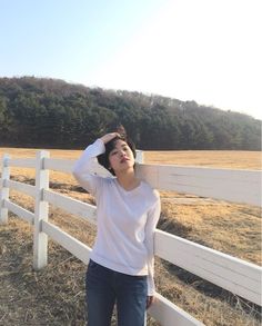 a woman standing in front of a white fence with her hands on her head and looking up at the sky