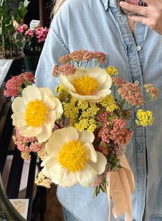 a woman holding a bouquet of flowers in front of her face and looking at her phone