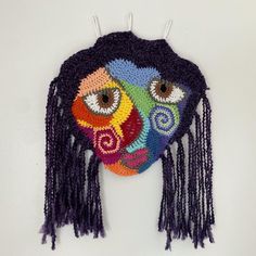 a crocheted mask hanging on the wall with eyes painted on it's face