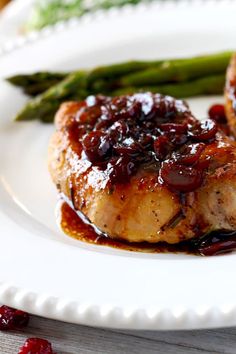 two pieces of meat on a plate with asparagus and cranberry sauce