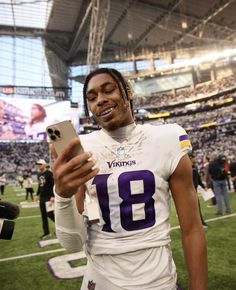 a football player holding a cell phone in his right hand and smiling at the camera