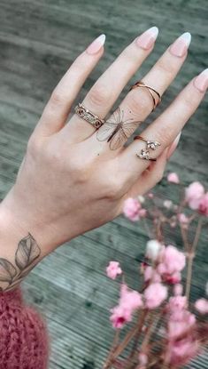 a woman's hand with three different rings on it and flowers in the background