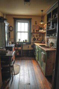 an old fashioned kitchen with wood flooring and green cabinetry, along with a large window