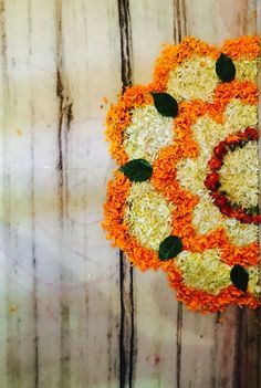 an orange and white flower arrangement with leaves on it's side, placed in front of a wooden wall