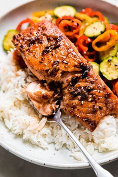 a white plate topped with rice and salmon next to vegetables on top of each other