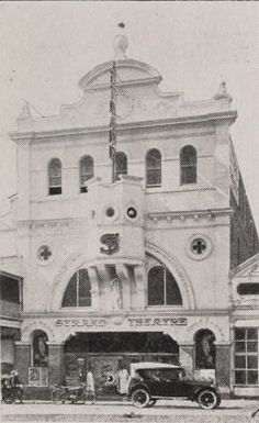 an old black and white photo of a car parked in front of a large building