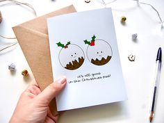 a hand holding a card with two christmas puddings