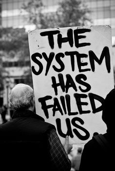 a man holding a sign that says the system has failed us