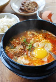 a bowl of soup with an egg in it and other dishes on the table behind it