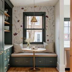 a window seat in a kitchen next to a table with flowers on it and a lamp hanging from the ceiling