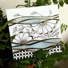 a white card with blue and gold designs on it next to a potted plant