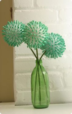 three flowers in a green vase sitting on a white counter top next to a brick wall