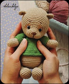 a person holding a small teddy bear in their hands with yarn on the ground behind them