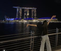 a woman standing next to a body of water with her arms outstretched in the air