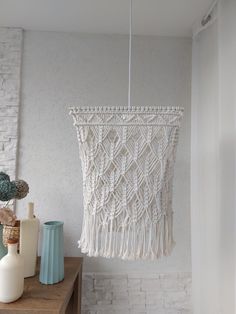 a white macrame hanging from the ceiling next to vases on a table