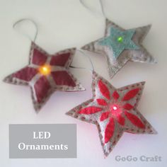 three christmas ornaments are hanging from strings on a white surface with green light in the middle