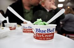 two people sitting at a table with ice cream in their hands and one person holding a spoon