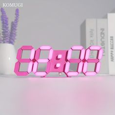 a pink digital clock sitting on top of a table next to a purple vase with flowers