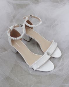 a pair of white shoes with pearls on the toes and heels are sitting on a veiled surface