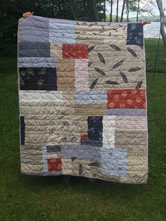 a quilt is hanging on a clothes line in front of some trees and grass with the water in the background