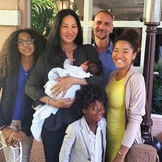 a group of people standing next to each other with a baby in their arms and smiling at the camera