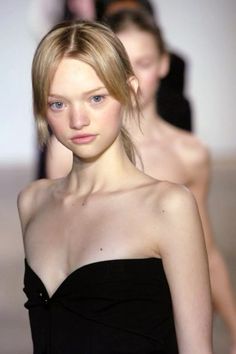 a model walks down the runway in a strapless black dress with her hair pulled back