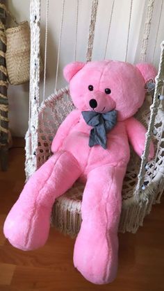 a pink teddy bear is sitting in a hammock with a bow tie on