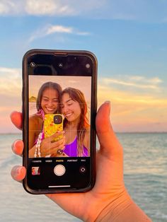 a person holding up a cell phone to take a selfie with the ocean in the background