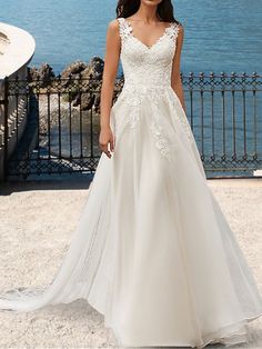 a woman in a white wedding dress standing by the water with her hand on her hip