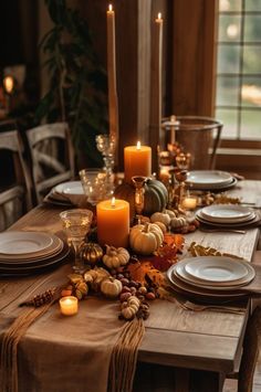 a table set with candles, plates and pumpkins