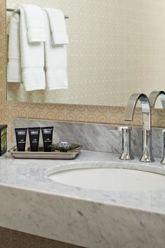 a bathroom with marble counter tops and white towels hanging on the wall above it, along with two personal care items