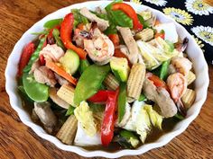 a white bowl filled with shrimp and veggies on top of a wooden table