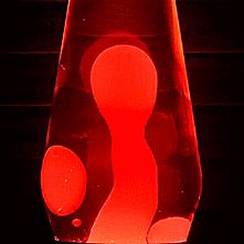 a red vase sitting on top of a black table next to a light that looks like a person's foot