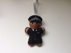 a teddy bear ornament with a police officer on it's back hanging from a silver ribbon