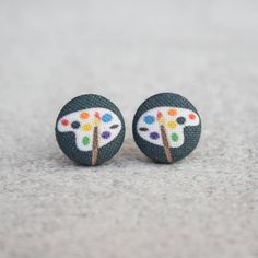 a pair of colorful earrings on top of a gray surface with white and black dots