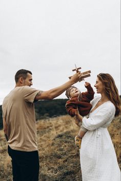 a man holding a baby while standing next to a woman in a field with an airplane