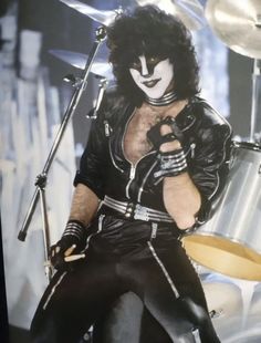 a man with black hair and white makeup holding a drum set in front of him