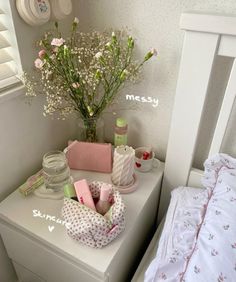 a white dresser topped with lots of items next to a bed covered in pink and white sheets