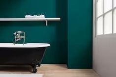 a bath tub sitting next to a white toilet in a green bathroom with wooden floors